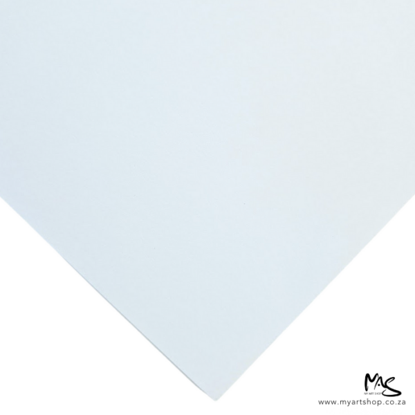 A single piece of paper from a Prime Art Soft Cover Creative Journal is shown in the frame. It is a close up of the corner of a sheet. The corner is shown diagonally, in the center of the frame. The paper is white and is on a white background.