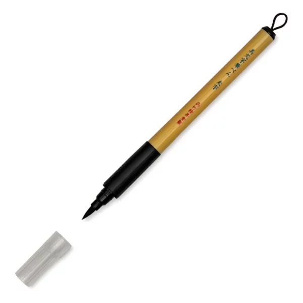 a single kuretake bimoji fude pen is in the center of the image at an angle. sitting diagonally across the screen from tip on the left bottom to the end on the top right corners respectively. it has a brown handle with a black top and a black bottom with a string on it. the nib is visable and the cap is sitting infront of it. on a white background