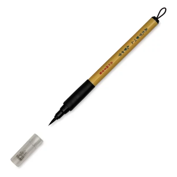 a single kuretake bimoji fude pen is in the center of the image at an angle. sitting diagonally across the screen from tip on the left bottom to the end on the top right corners respectively. it has a brown handle with a black top and a black bottom with a string on it. the nib is visable and the cap is sitting infront of it. on a white background