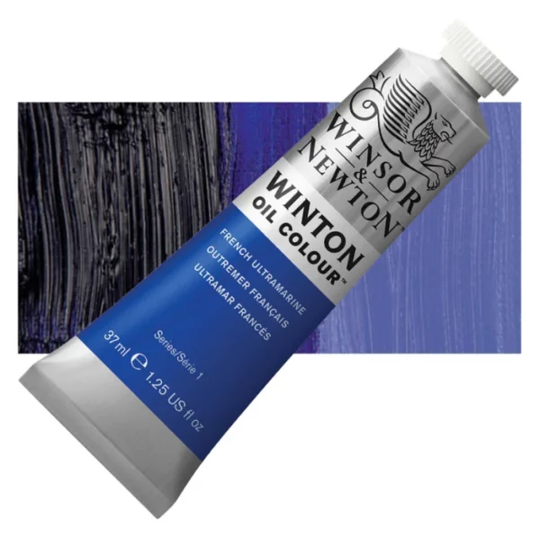 A tube of French Ultramarine Winsor and Newton Winton Oil Paint 37ml is shown diagonally, across the center of the frame. The tube is a silver colour and has a white screw on, plastic lid. The Winsor and Newton logo is printed at the top of the tube and there is a white band printed across the tube, below the logo, that has the words 'Winton Oil Colour' written on it. Below that is a colour band printed across the tube that has black text describing the product colour and paint properties. There is a rectangular colour swatch behind the tube that shows the colour of the paint. It lays horizontally across the top third of the frame. The image is center of the frame and on a white background.