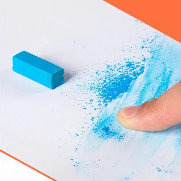 A single Mungyo Soft Pastels is seen laying on a piece of white paper. The pastel is blue and short and rectangular in shape. A persons hand can be seen coming into the frame from the bottom right hand corner. They are using their finger to smudge some blue pastel across the paper.