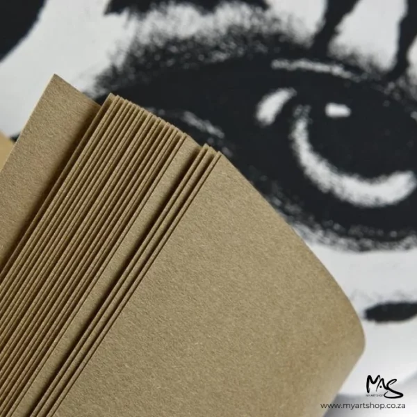 A close up of the sheets of paper inside the Sand Fabriano Toned Paper Pad. The sheets are being pulled back so you can see them slightly folded and showing multiple sheets within the pad. There is a picture of a zebras eye in the background. The image is cut off by the frame.