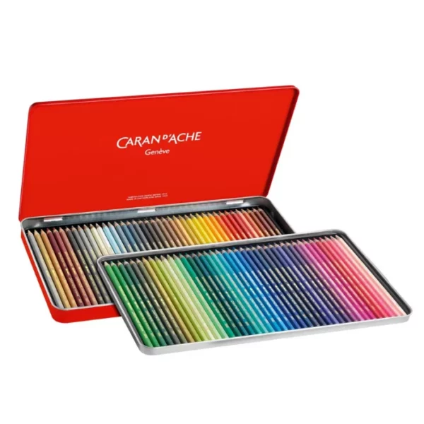 A Set of 80 Caran D'Ache Supracolor Pencils is shown with the hinged lid open, in the center of the frame horizontally. The pencils are encased in a red tin with the Caran D'Ache name printed on the inside of the tin lid. The pencils are lined up neatly next to each other in the base of the tin. Each pencil is a different colour and the pencil barrels reflect the colour of the pencil lead. On a white background.