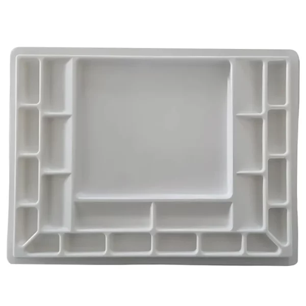 The base of a Sterling Edwards Big Brush Palette is shown horizontally, across the center of the frame. The palette is white plastic and has 14 wells of different sizes. The image is center of the frame and on a white background.