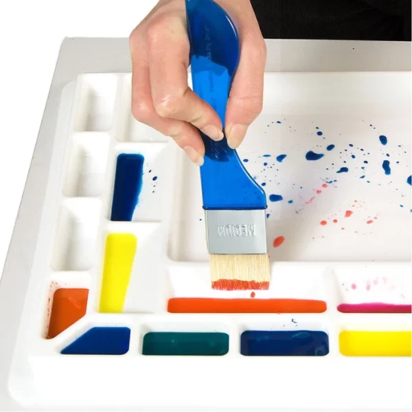 A close up of a persons hand dipping a paint brush into a Sterling Edwards Big Brush Palette. The wells are large enough for big brushes. The palette is made of white plastic and has 14 different wells. On a white background.