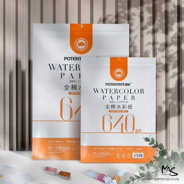 There are 2 packs of Double Sided Potentate Watercolour Paper shown next to each other, a front view of the packets. The one on the left is larger than the one on the right. The packets are white and contain the paper inside. The packets have an orange band around the bottom of them. There is text on the packets describing the quality of the papers. There is a slatted wall in the background and some tubes of watercolour paint scattered in front of the paper packs.