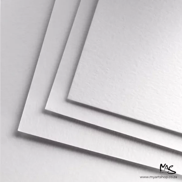 A close of up loose sheets of paper found in the Fabriano Mixed Media Pads. There are 3 sheets, staggered on top of each other. The image is a close up of the corner of the papers. They are white and are cut off by the frame.