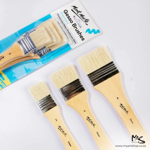 There is a full set of Mont Marte Discovery Gesso Brushes coming in diagonally from the top left hand side of the frame. There are 3 loose brushes below that. The largest brush is to the right, the medium sized brush is in the middle and the smallest brush is to the left. They are laying on a white background and it is a birds eye view. The image is cut off by the frame.