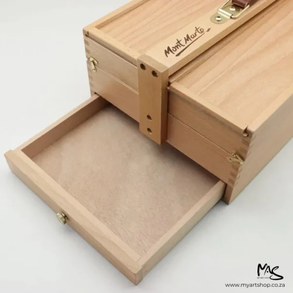 A Mont Marte Signature Multi Purpose Art Box is seen coming into the frame from the top right hand side. The box is closed, with a single tray open at the bottom of the box. The image has a light grey background.