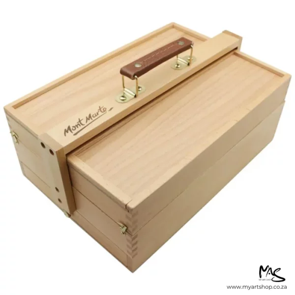 A single Mont Marte Signature Multi Purpose Art Box is shown diagonally across the frame. The view is angled and is of the side and top of the box. The box is wooden and has a leather carry handle. The image is center of the frame and on a white background.