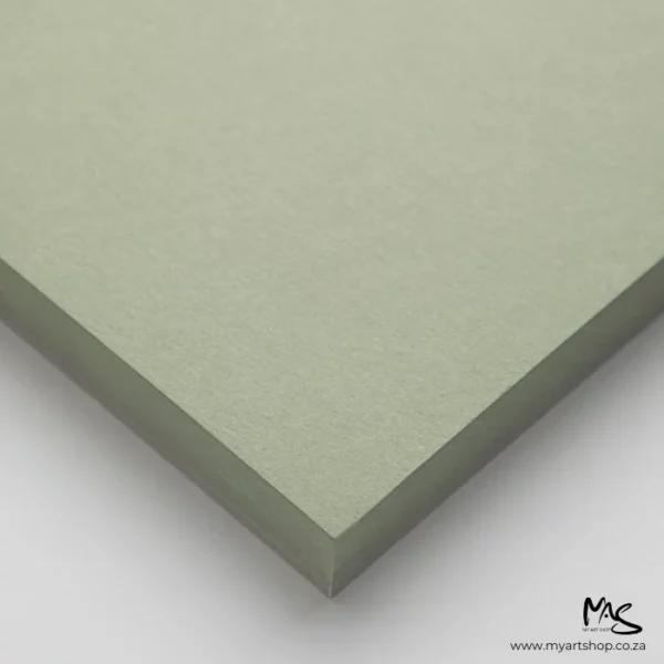 A close up of the corner of a pile of papers from the Moss Fabriano Toned Paper Pad. The corner of the papers is pointing towards the center of the frame. The paper is green and on a light grey background.