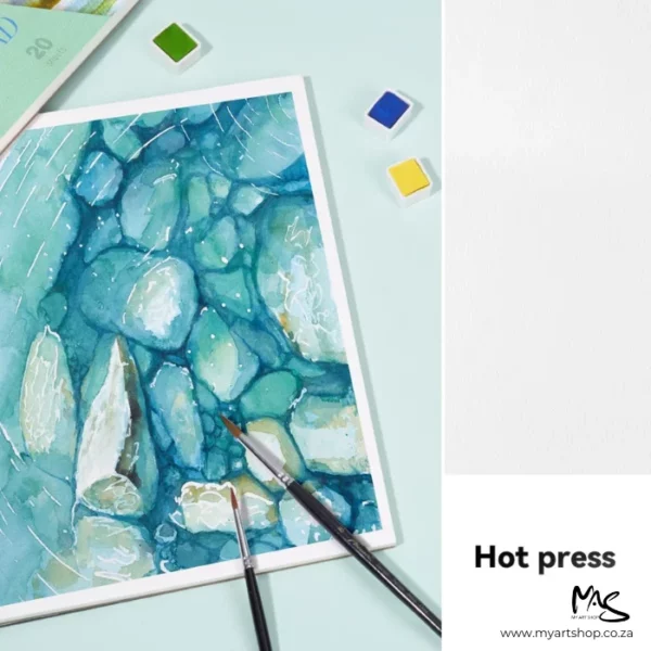 A promotional image for Hot Press Potentate Watercolour Blocks. There is a painted picture of stones under water along the left hand side of the frame, with 2 paintbrushes leaning on top of the painting at the bottom of the frame. There are a few watercolour pans around the picture. There is a piece of white paper vertically, down the right hand side of the frame, which shows the grain of the paper and text in the bottom right hand corner of the frame describing the type of paper.