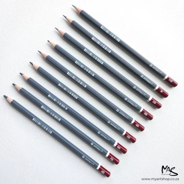 Prime Art Graphite Pencil Set. 9 pencils are laying diagonally across the center of the frame. The pencils have a maroon tip with the grade printed in white and a dark grey barrel. The maroon ends are facing the right hand side of the frame and the lead tips are facing towards the top left hand corner. They are on a light grey background with a canvas texture.