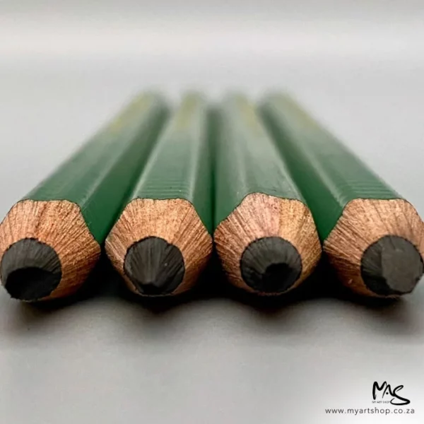 Four 9XXB Kimberley Drawing Pencil from the General Pencil Co. are shown laying on a surface. The image is taken of a close up of the pencils from the lead tips and the back of the image is blurred. The pencils have a green barrel and are on a light grey background.