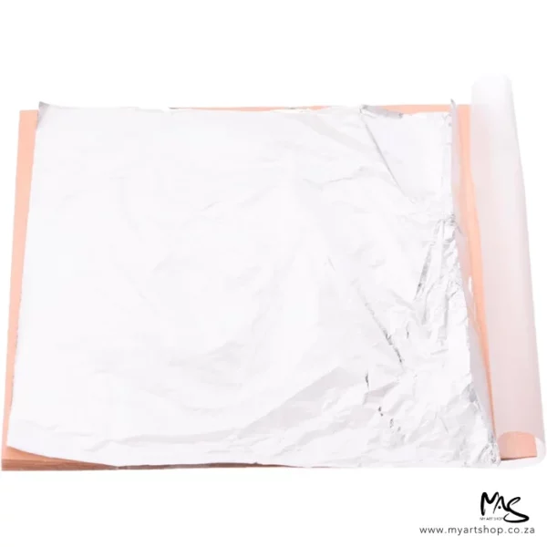 An open pack of Mont Marte Imitation Silver Leaf can be seen in the center of the frame. The sheets are silver and there is a peach coloured paper between the sheets. The image is on a white background.