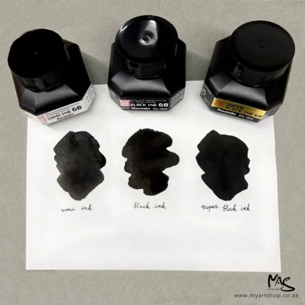 Three bottles of ink are shown without lids. One bottle is ZIG Cartoonist Sumi Black Ink. They are sitting on a piece of white paper and there is a sample from each bottle on the white paper.