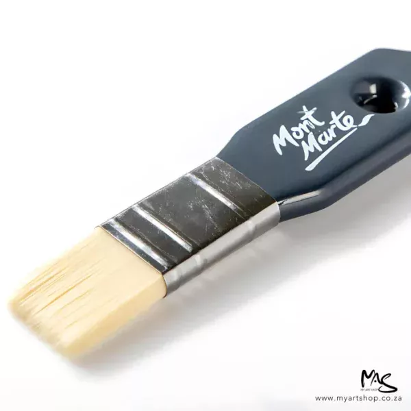 A close up of a Mont Marte Abstract Expression Brush 25mm. The brush is coming into the frame, diagonally, from the right hand side of the frame. The brush has a grey plastic handle with the Mont Marte logo printed on it and natural coloured bristles. On a white background.