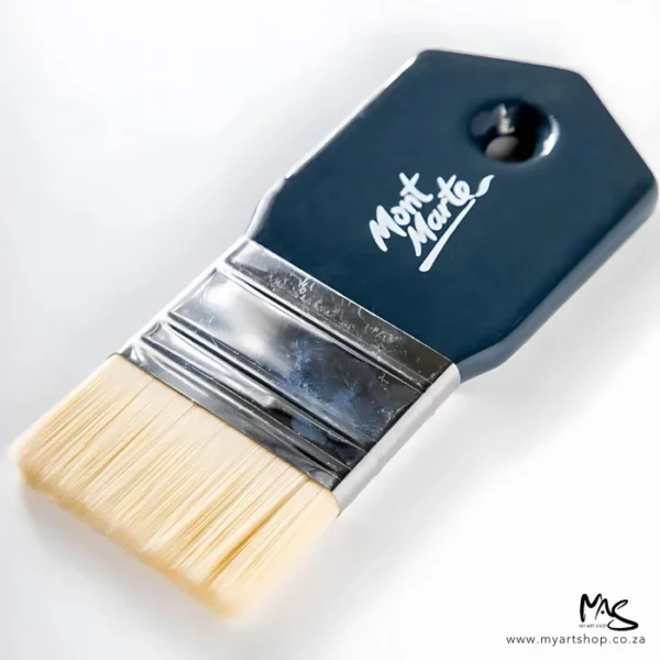 A close up of a Mont Marte Abstract Expression Brush 50mm. The brush is coming into the frame, diagonally, from the right hand side of the frame. The brush has a grey plastic handle with the Mont Marte logo printed on it and natural coloured bristles. On a white background.