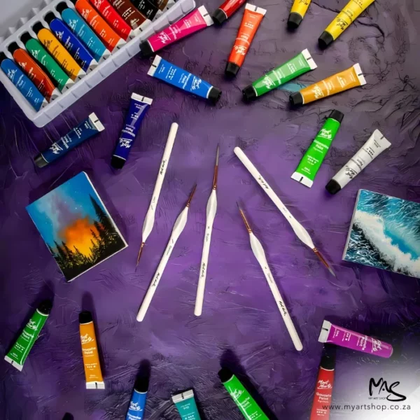A promotional image for the Mont Marte Detail and Liner Brush Set 5 piece. The detail brushes are shown in the center of the frame, scattered on a purple background. There are various tubes of Mont Marte paint around the frame.