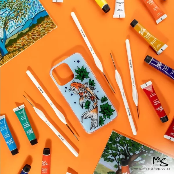 A promotional image for Mont Marte Detail and Liner Brush Set 5 piece. The brushes are scattered around the center of the frame. There is a cell phone cover in the center that is painted with a fish. there are various tubes of Mont Marte paint scattered around the brushes. On an orange background.