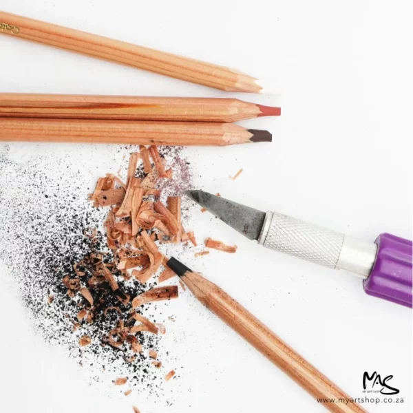 Loose pencils from the Mont Marte Signature Coloured Charcoal Pencil Set are seen scattered within the frame with a kraft knife and pencil shavings showing that you use a craft knife to sharpen them. The image is cut off by the frame.