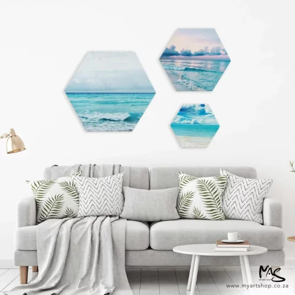 There are three Dala Hexagonal Stretched Canvases hanging on a wall behind a couch that has cushions and a blanket thrown over it. The canvases have pictures of an ocean theme.