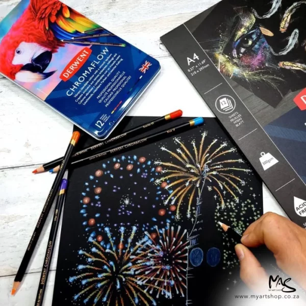 A promotional image containing a Set of 12 Derwent Chromaflow Pencils laying on a drawing of fireworks that has been made on black paper using the pencils from the set. The image is cut off by the frame.