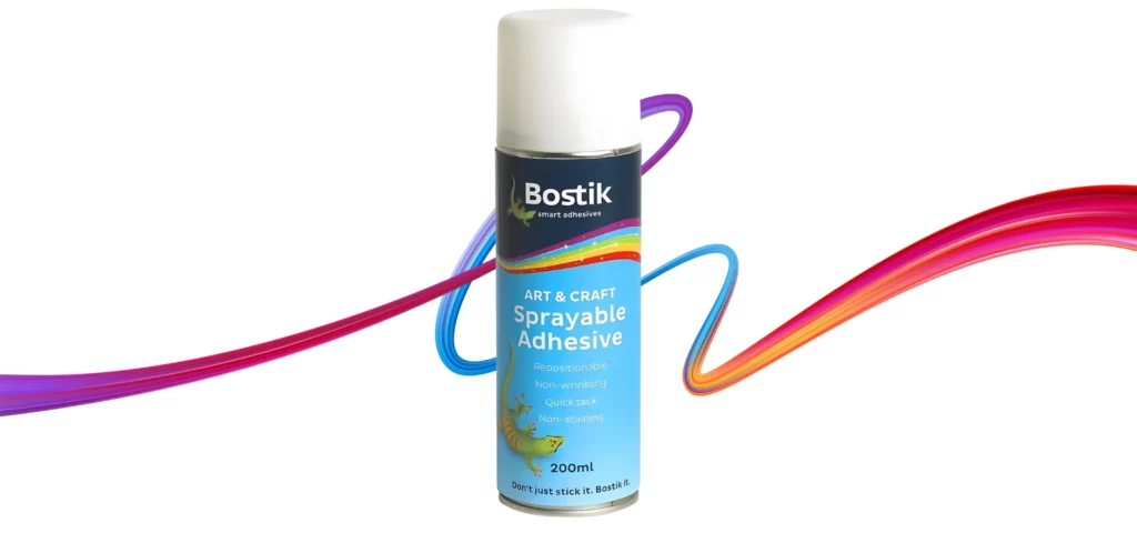 bostick spray adhesive is sitting in the center of the image. it is a blue can with white writing and a rainbow line across the top. it has a white lid. it is sitting infront of a rainbow squiggle and is on a white background