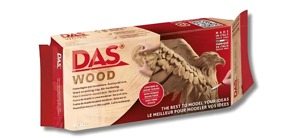 DAS Wood. A single slab of das wood in its packaging is showing center of the frame, hosizontally at a slight angle with a drop shadow. The packaging is red and brown and has a picture of an eagle that has been carved out using the wood clay. There is text on the front of the packaging.