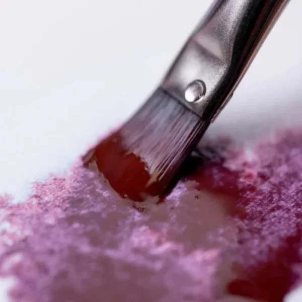 A close up of a paint brush painting a deep red colour onto a piece of watercolour paper. The paint used is from the Granulating Gansai Tambi Watercolour Set.