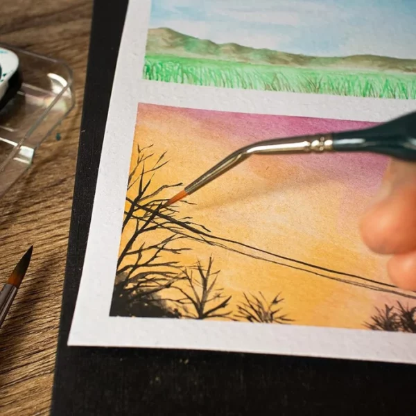 A close up of a persons hand that is coming in from the right hand side of the frame, holding a brush from the Mont Marte Fine Detail Brush Set. They are painting a fine line with the brush.