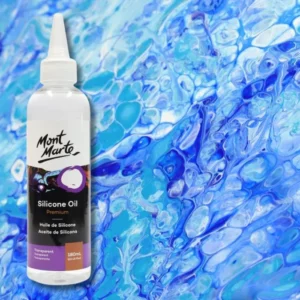 A bottle of Mont Marte Premium Silicone Oil is shown along the left hand side of the frame. The bottle is white plastic with a label around the body of the bottle that is printed with text and the Mont Marte Logo. The bottle has a nozzle top and cap. The bottle is shown over laying a background of blue paint that has been poured and cells have created.