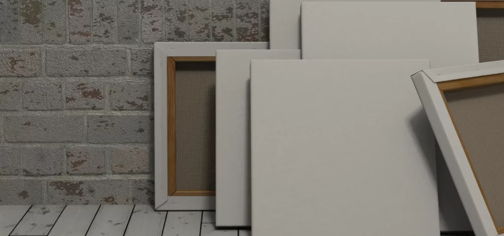 a variety of canvas is stacked in a room. the wall is white washed brick that its leaning on and the floor is white wood