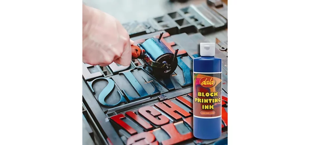 Dala Block Printing Inks/ A close up of a persons hand using a brayer to adhere ink to the surface of typography letters. They are adhering blue and red ink. There is a bottle of blue ink in the bottom right hand corner of the frame, superimposed over the image. The bottle is clear plastic with a white flip cap lid and a printed lable. The bottle of ink is blue.