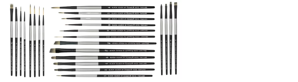 in the center of the image or a variety of shapes and sizes of the black silver brushes. all lying horizontally hairs facing the left hand side. they have beige hair, black ferrules and black and silver stems. on either side are the ame brushes but standing vertically next to the horizontal ones. all on a white background