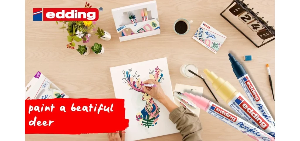 in the center of the image there is a persons hand drawing on a canvas a picture of a deer in multiple different colours. on a wooden desk with different edding pens scattered around them and the label coming off the left side of the image saying edding.