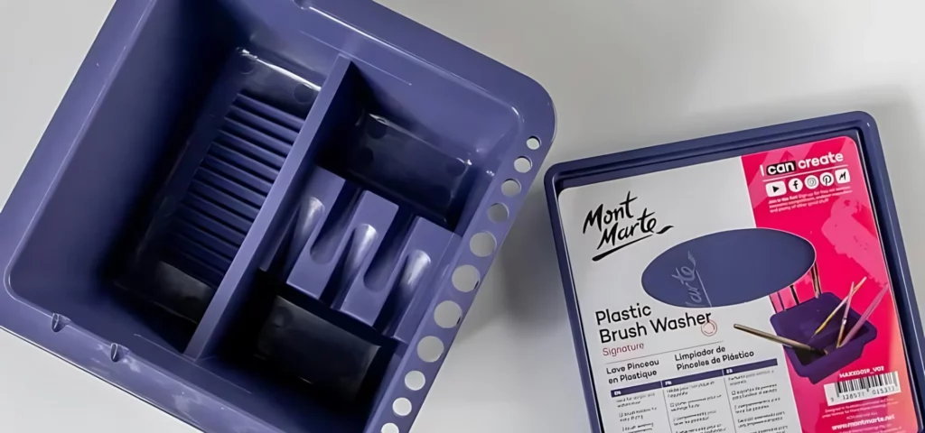 Mont Marte Signature Plastic Brush Washer. The base of the brush washer is placed to the left hand side of the image and shows a top view of the brush washer, looking into the the brush washer from above. The lid id placed to the right hand side of the base and has the label attached to the top of the lid. On a white background.