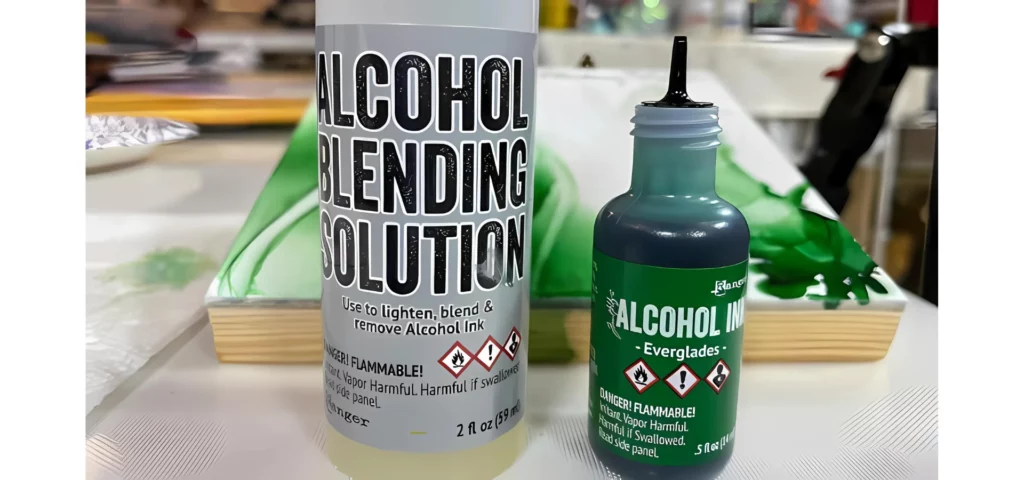 in the front center of the image on the left hand side is a bottle of blending solution and next to it is an open bottle of green alcohol ink. they are standing upright in front of a yupo that has the green ink on it. on a wooden tabletop