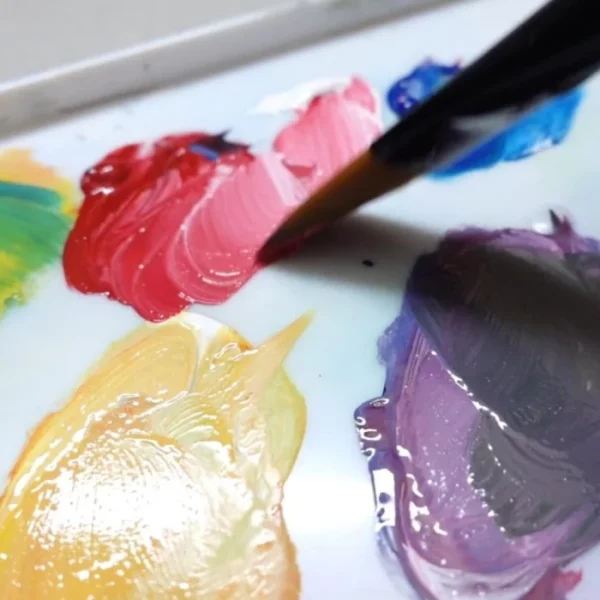 A close up of a paint brush being dipped in a palette that has Caran D'Ache Studio Gouache Paint.