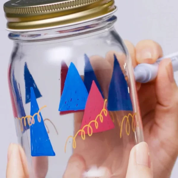 A close up of a persons hand holding a Copic Acrea Paint Marker, drawing on a gladd jar. They are drawing triangles and squiggles.