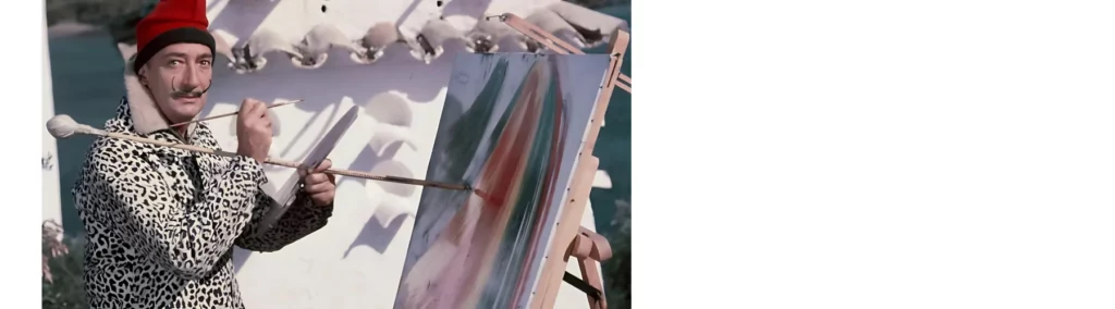 in the center of the image is a picture of artist salvitore dali. he has a red hat on and a long moustache that is curved upwards by his cheeks. he is using a mahle stick to balance on while he paints a large canvas that is infront of him. he is outside in the image and the sund is shining on him