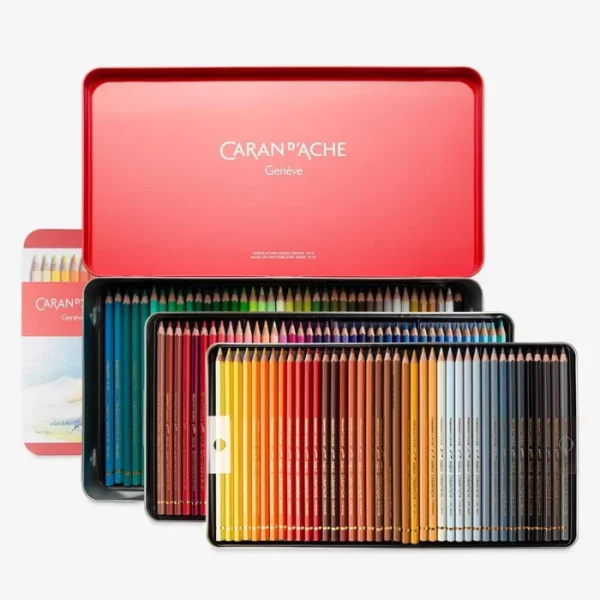 A Set of 120 Caran D'Ache Pablo Coloured Pencils is shown in the center of the frame. The set is opened and there are 3 trays of pencils that are shown coming out of the red tin. The tin lid is open and the Caran D'Ache logo is printed inside the tin in white. The pencils are lined up next to each other in each tray. They have a coloured barrel that depicts the colour of the pencil. On a light grey background.