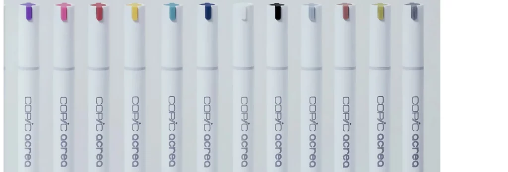 12 copic acrea markers are lined up in a row across the image. the caps have a little colour bit on them showing what colour is in each pen. the background is white