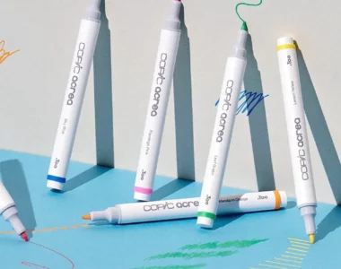 acrea-paint-markers-splash-scribble-create. There are 6 Copic Acrea Paint Markers shown in the frame. They are standing up against a wall that has been drawn on using the markers.