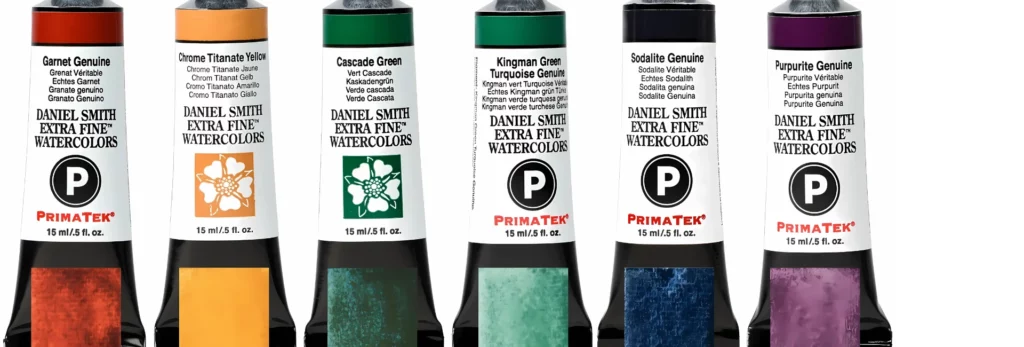 the image is a close up of 6 daniel smith watercolour tubes all lined up with a colour swatch on watercolour paper in a strip coming up underneath on on them. they are on a white background. the tubes are: red, yellow, green. blue and purple