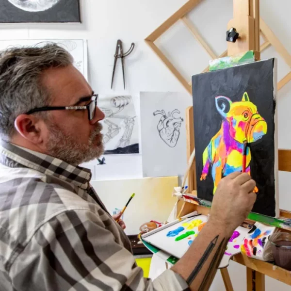 A man is seen painting an image of a dog using the Fluoro Mont Marte Premium Acrylic Paint Set. The dog is fluorescent and multi coloured.