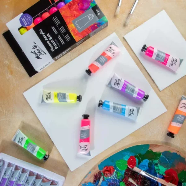 A promotional image for the Fluoro Mont Marte Premium Acrylic Paint Set. The tubes of paint are scattered around the frame, on top of white canvas boards, There is a full set at the top of the frame. It is a birds eye view.