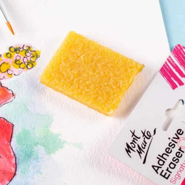 A close up of the Mont Marte Signature Adhesive Eraser laying on a piece of watercolour paper that has been painted. The image is cut off by the frame. The eraser is yellow in colour and textured and rectangular in shape.