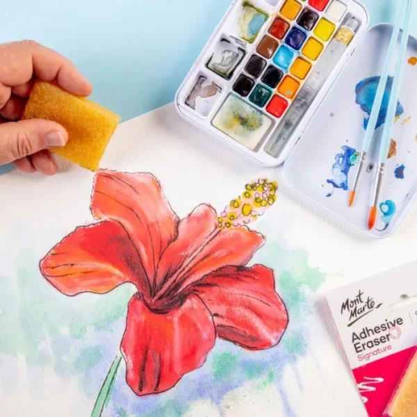 A close up image os a person using the Mont Marte Signature Adhesive Eraser to erase adhesive from a painting of a red flower. There is a paint palette in the top right hand corner of the image. The image is cut off by the frame.