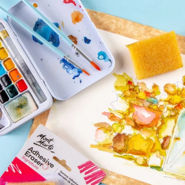 A Mont Marte Signature Adhesive Eraser is seen laying on a piece of watercolour paper that has been painted. There is an abstract image painted on the paper. There is a watercolour paint tin in the top left hand corner of the frame. The image is cut off by the frame.